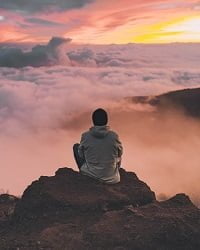 Man from the back, sitting on a rock looking at clouds