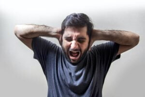 man covering his ears and screaming with anger