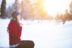 A woman sitting down with eyes closed, praying in winter.