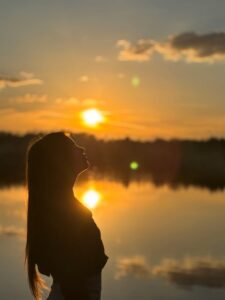 Silhouette of a woman at sunset by a calm lake, symbolizing inner peace and emotional resilience.
