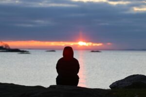 Person sitting quietly by the sea reflecting, symbolizing healing, compassion, and connection during difficult times